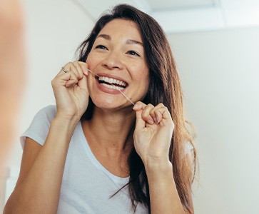 Woman smiling while flossing in bathroom
